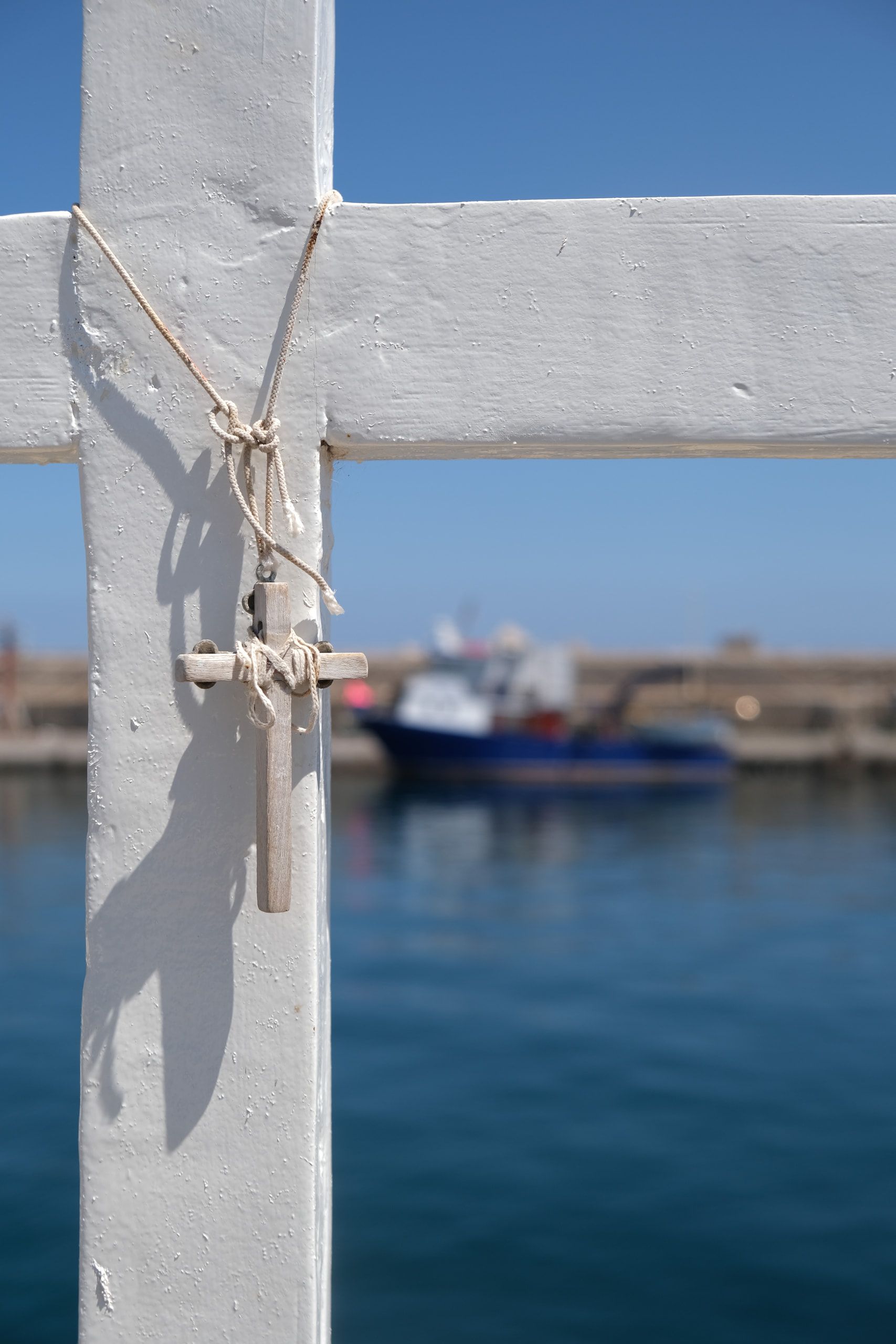 Una corda annodata a un palo, con il mare e una barca ormeggiata sullo sfondo