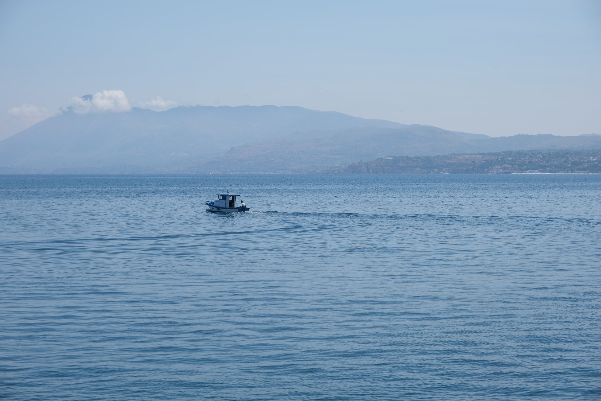 Una piccola barca attraversa il mare calmo, con i monti velati di foschia all'orizzonte