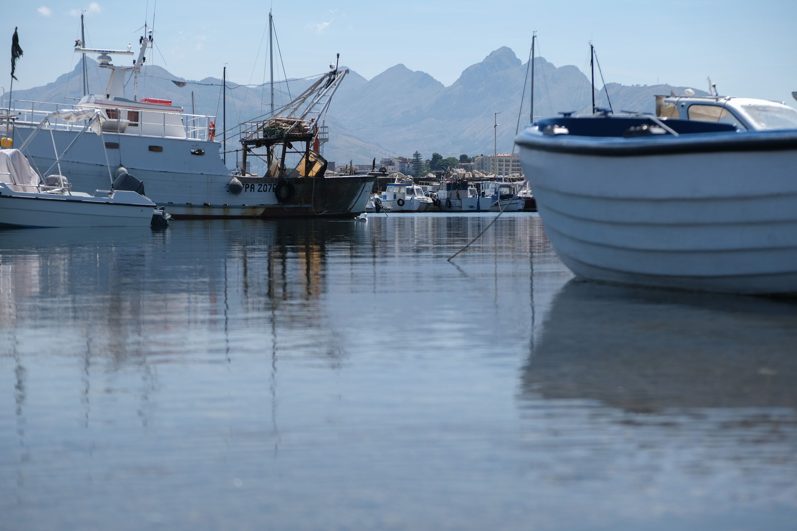 Alcune barche ormeggiate si specchiano nell'acqua ferma del porto, con i monti sullo sfondo