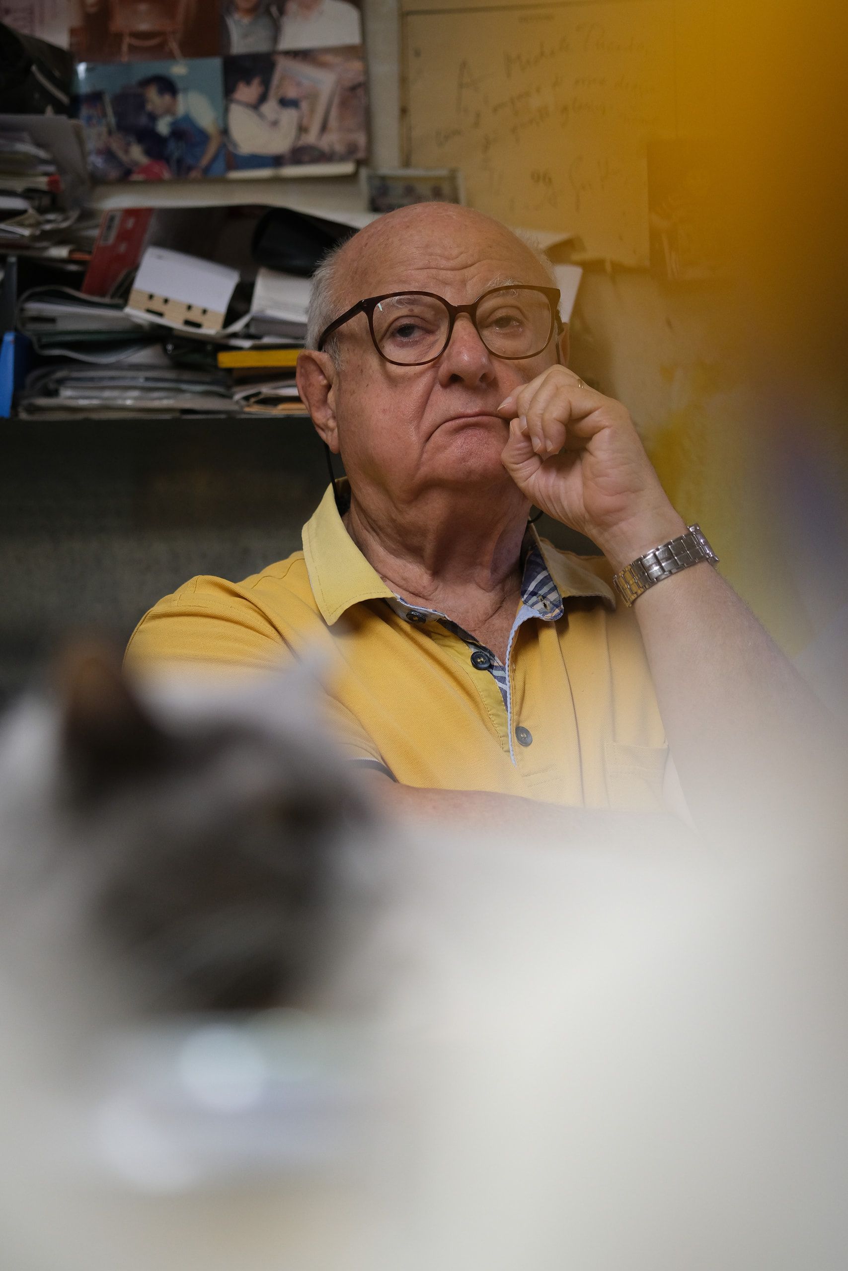 Un ospite anziano della bottega ascolta con la mano sul mento, dietro un gatto sfocato