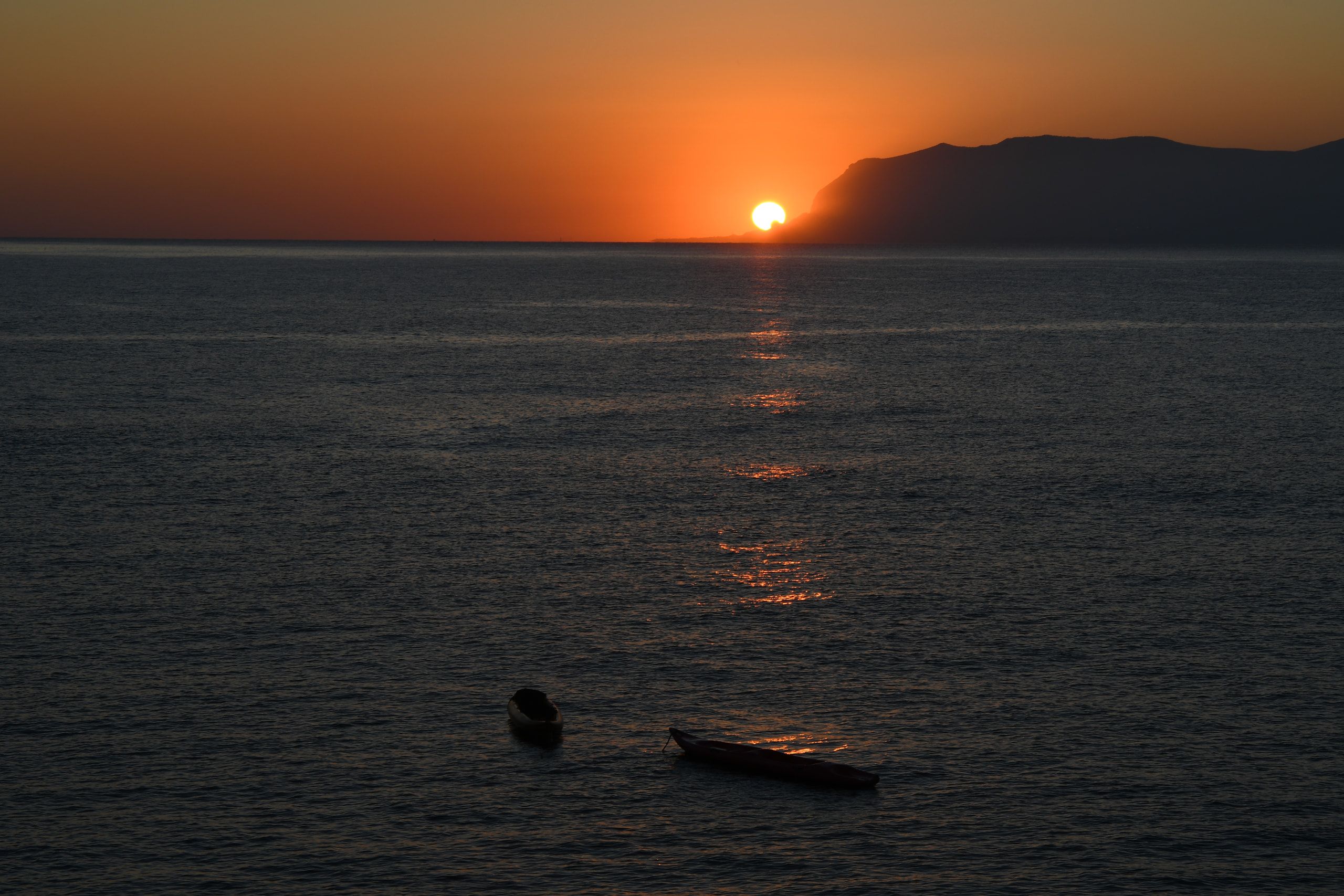 Il sole sorge sull'orizzonte del mare accanto a un promontorio, con due canoe ferme in primo piano