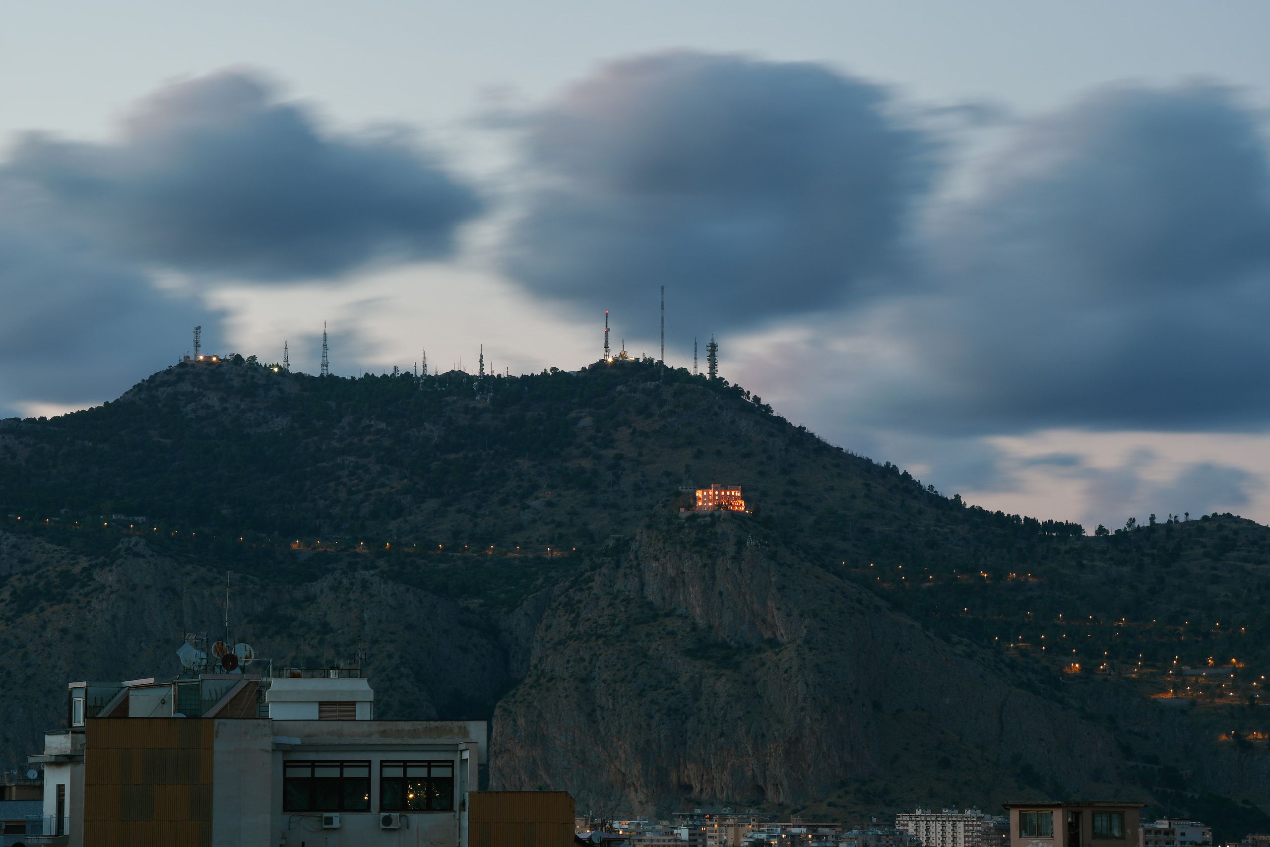 Monte Pellegrino con antenne sulla cima e il Castello Utveggio illuminato sul costone, sotto nuvole mosse, al crepuscolo