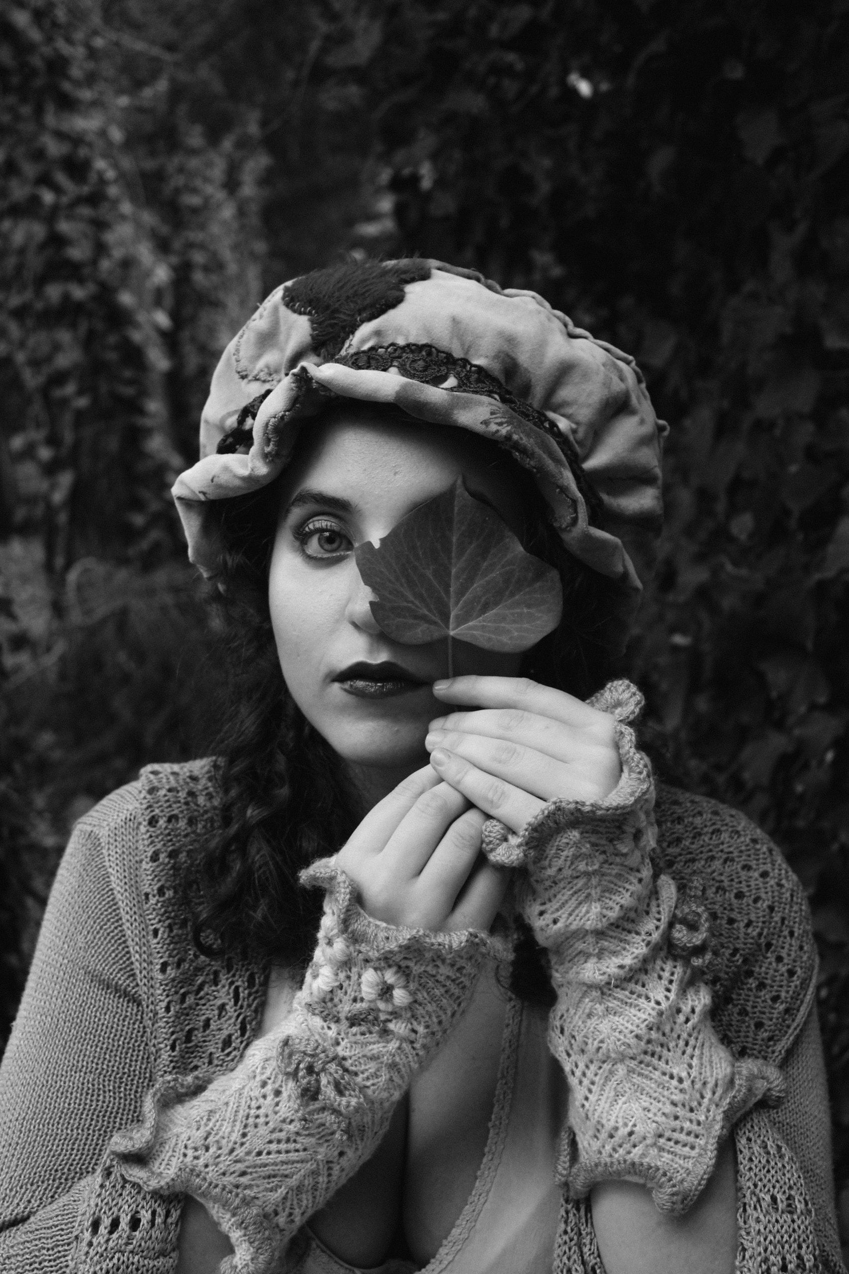 Una donna con un cappello di stoffa e guanti a maglia senza dita si copre metà del viso con una foglia