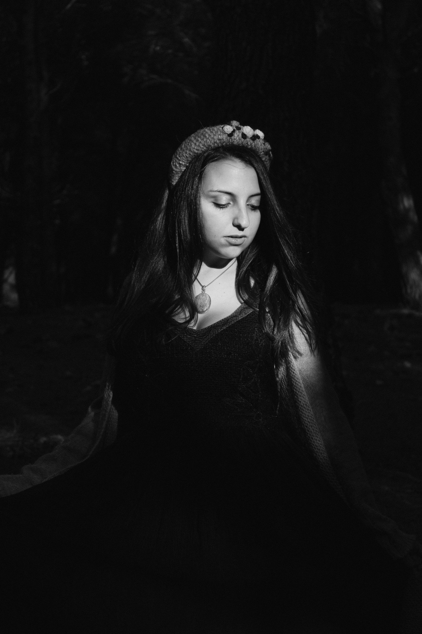 Una donna in abito scuro abbassa lo sguardo, colpita da una lama di luce nel bosco
