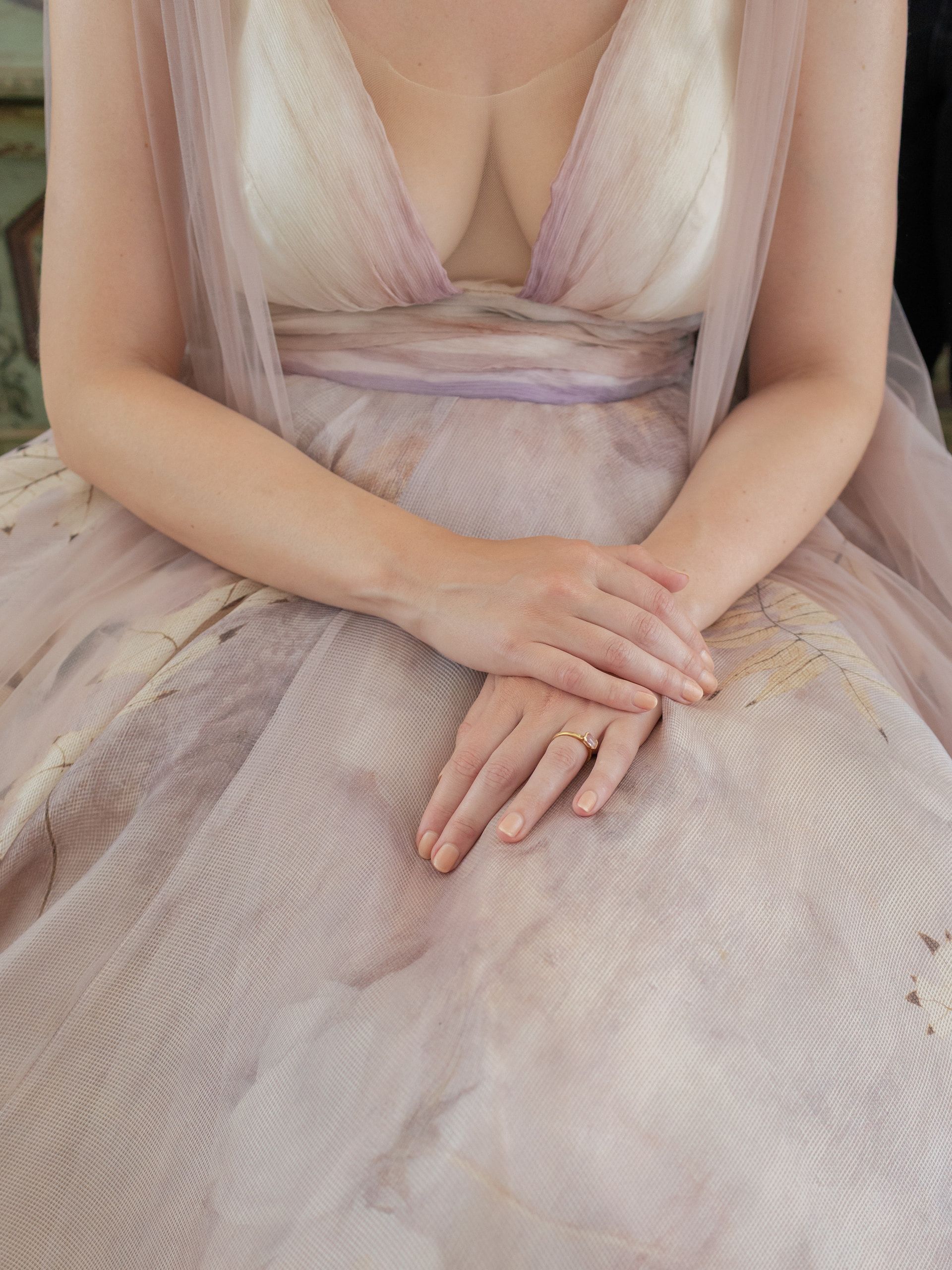Le mani della sposa posate in grembo sul vestito di tulle rosa e lilla