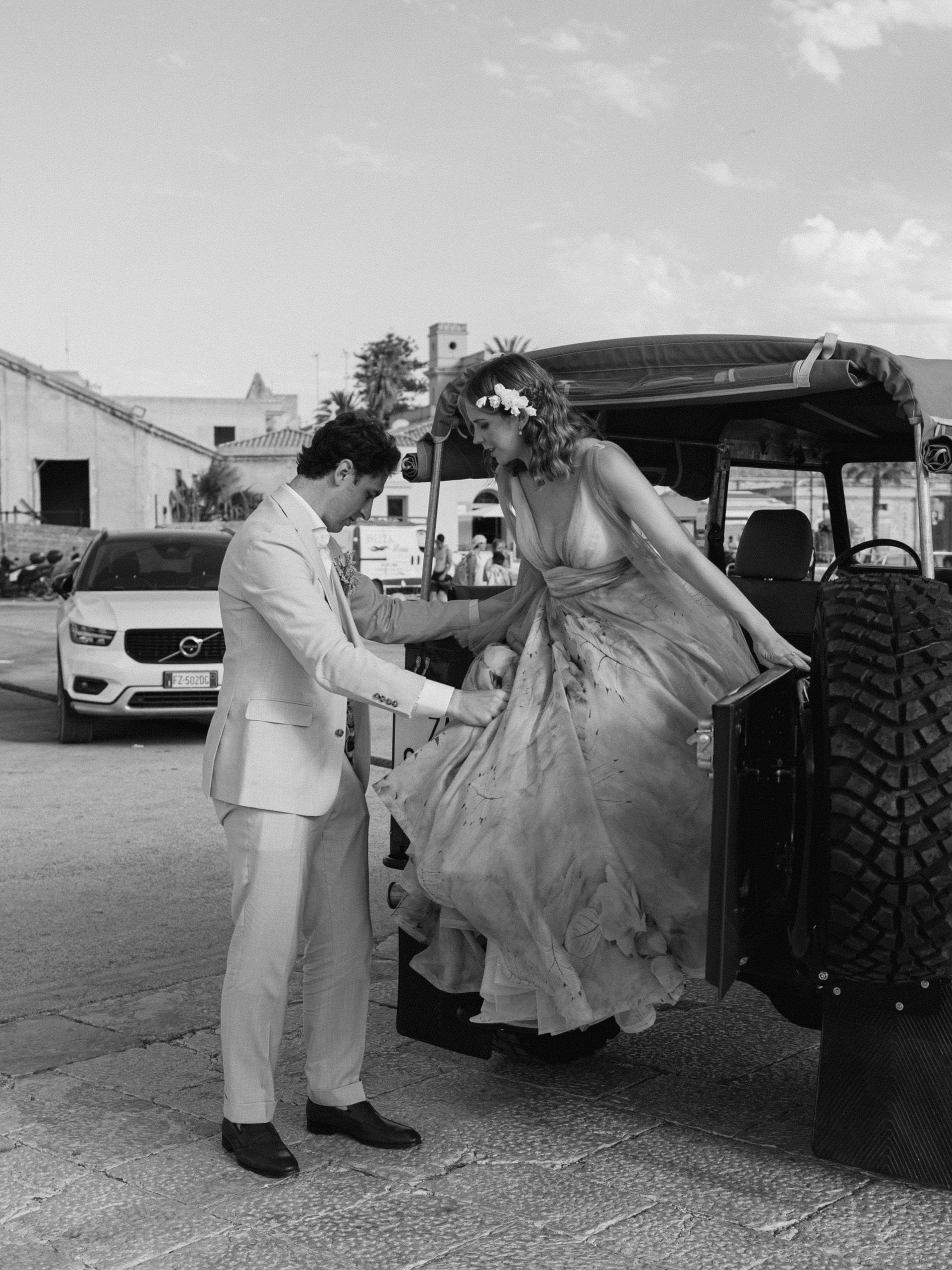 In bianco e nero, lo sposo aiuta la sposa a scendere dalla jeep