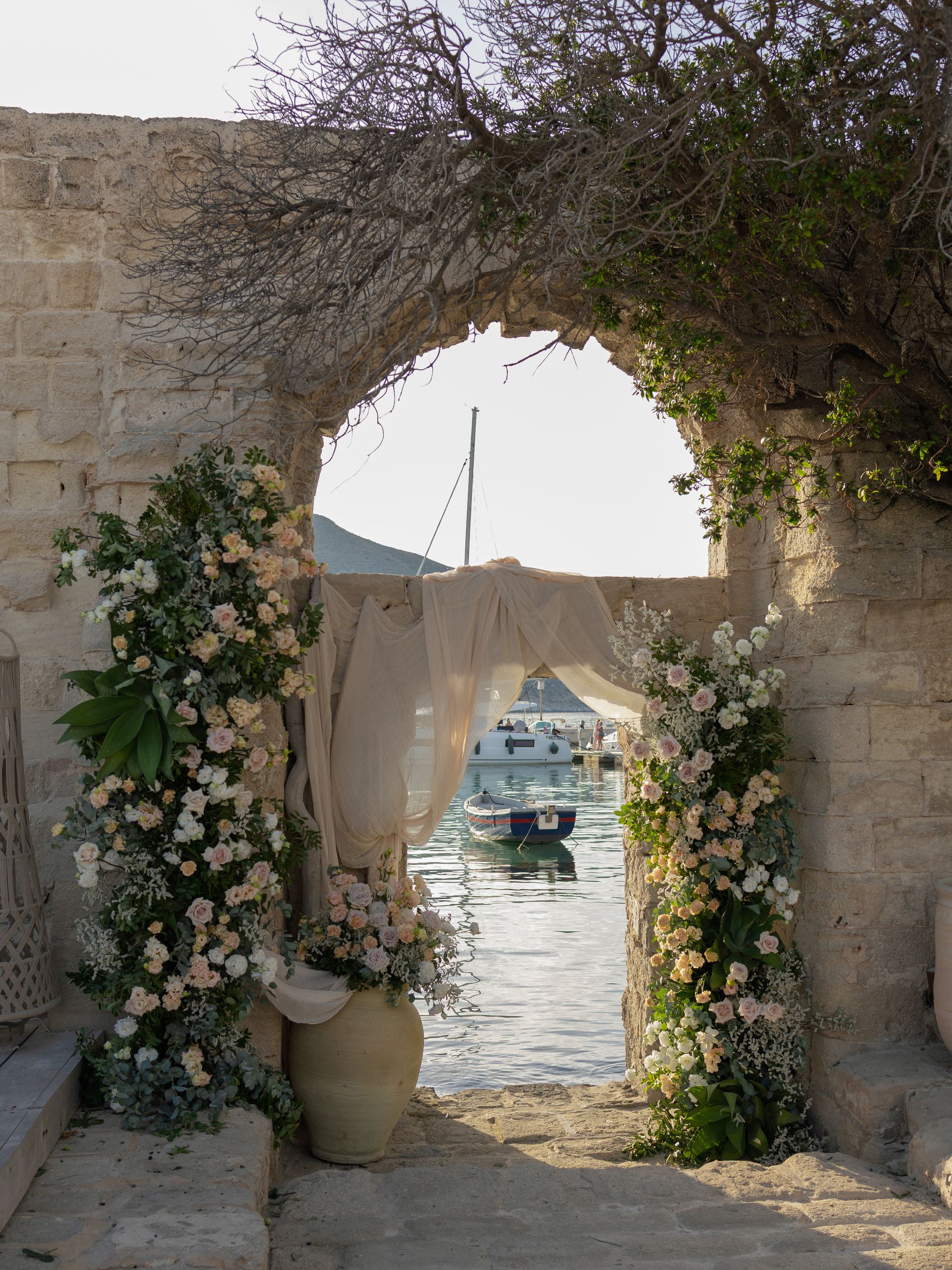 L'arco di pietra della cerimonia, con i fiori e i drappi, aperto sul mare e su una barca ormeggiata