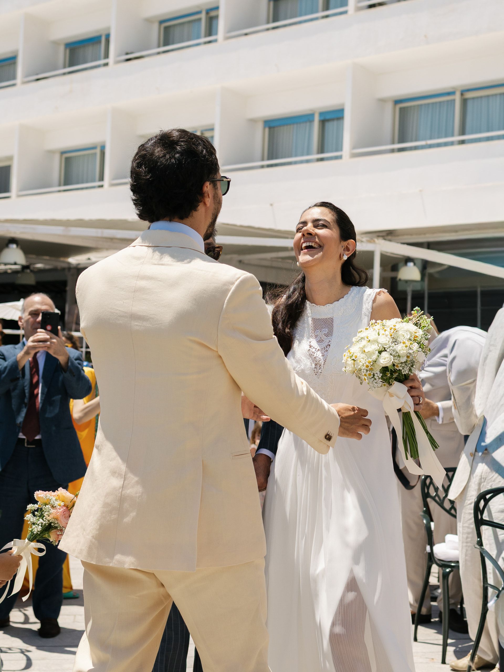 Lo sposo, di spalle, accoglie la sposa che ride con il bouquet di fiori bianchi