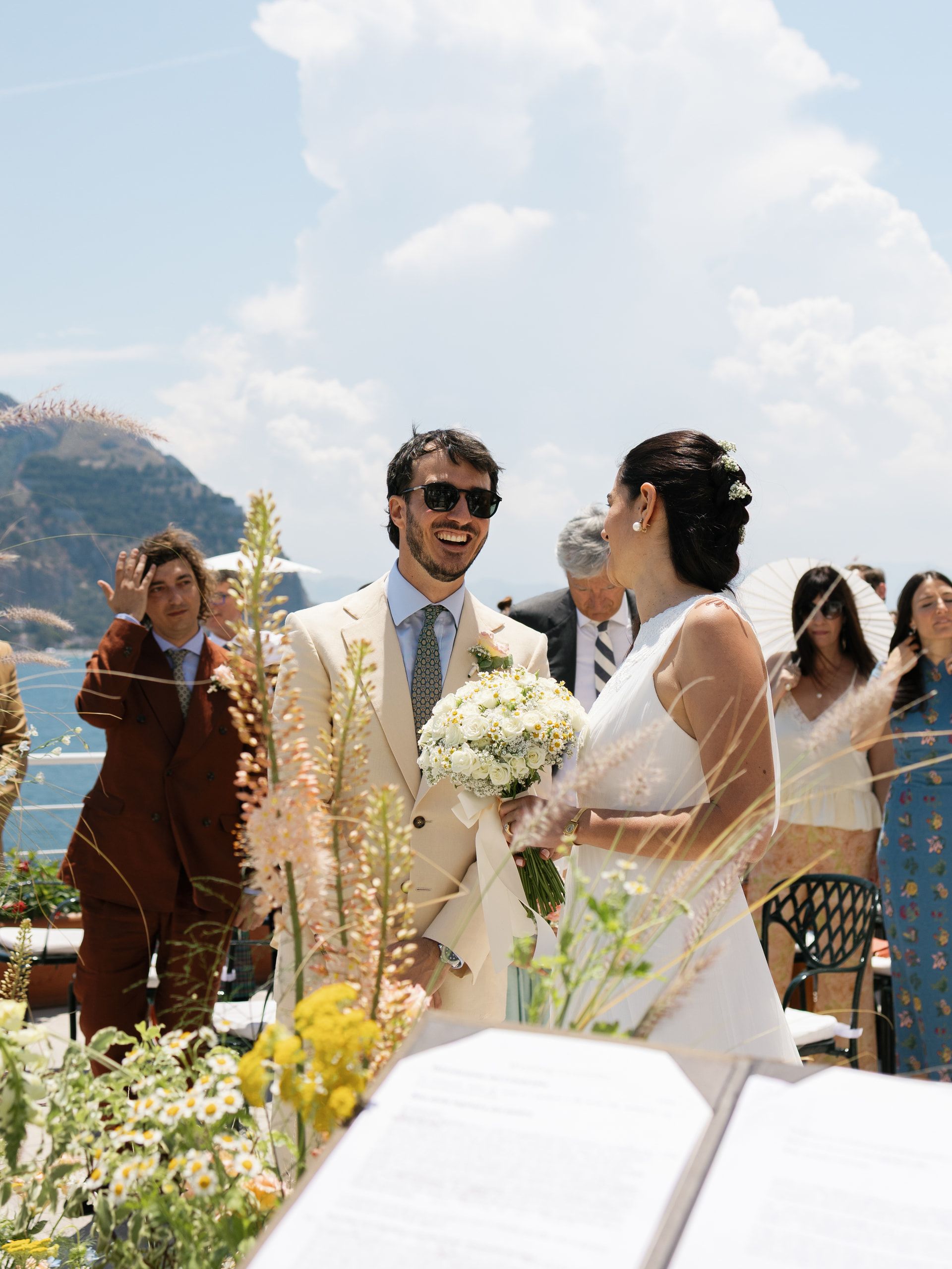 Gli sposi davanti al leggio della cerimonia, la sposa con il bouquet, gli invitati intorno