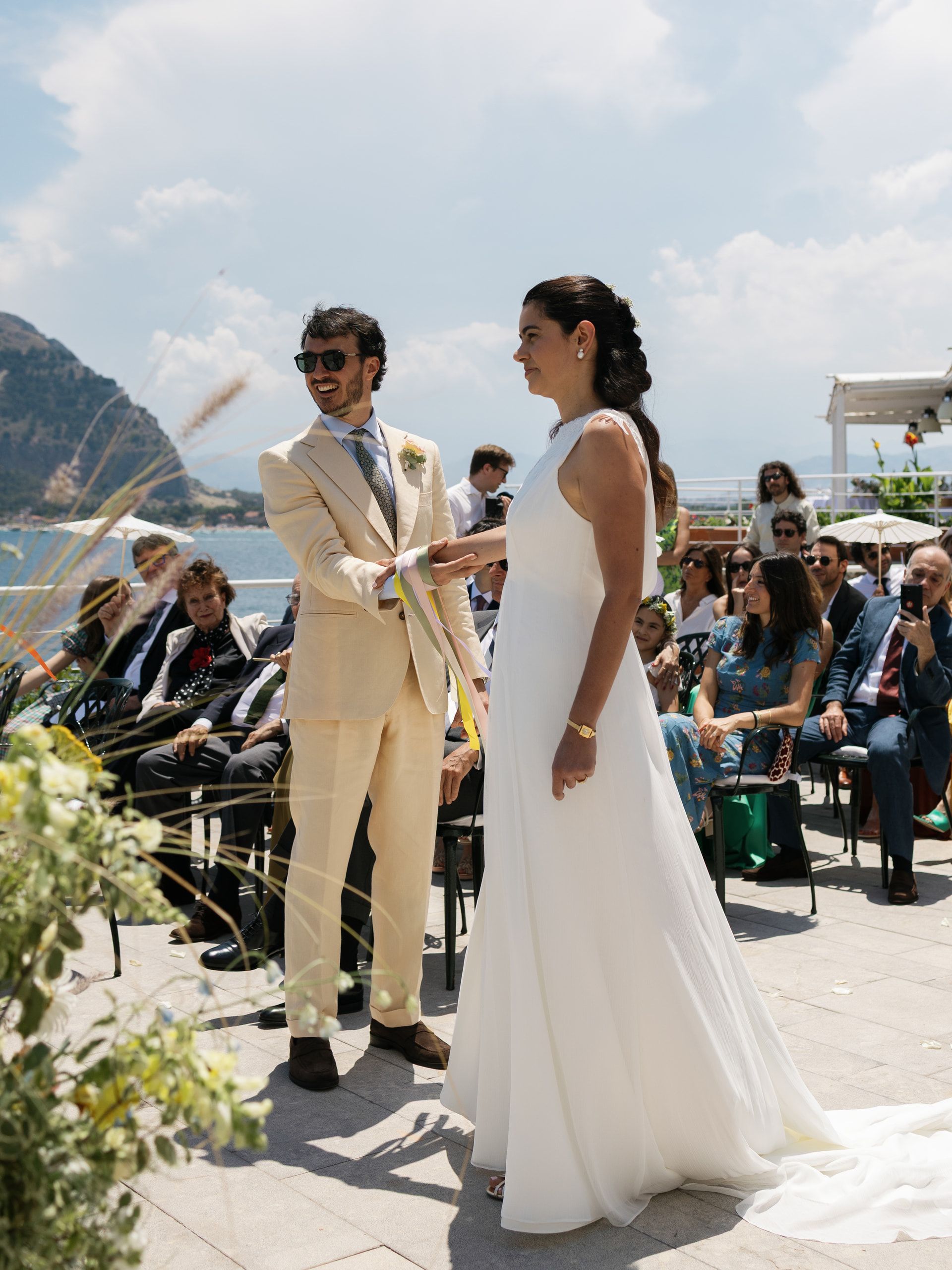 Gli sposi in piedi l'uno di fronte all'altra durante la cerimonia, con il golfo e il promontorio alle spalle