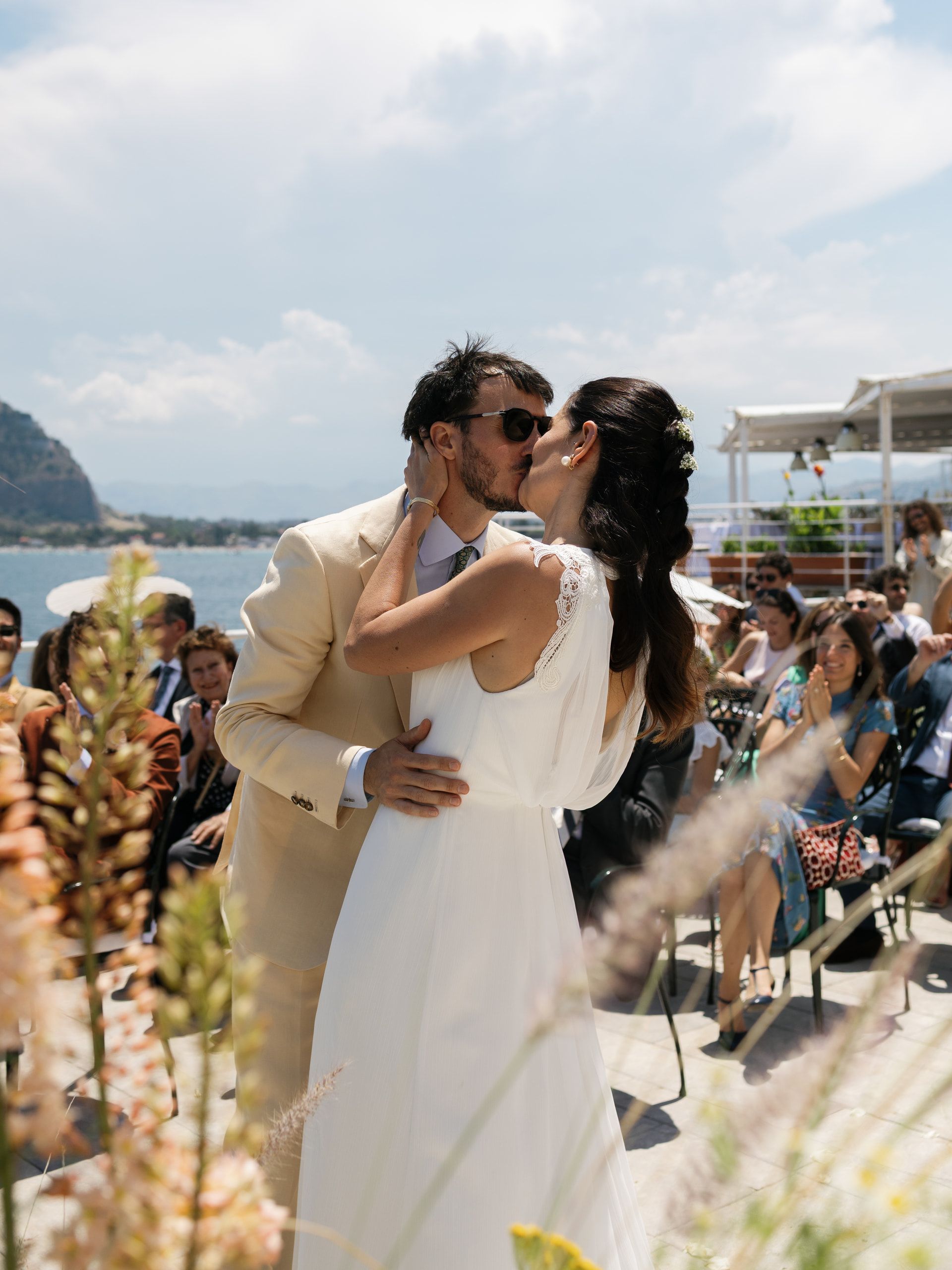 Gli sposi si baciano dopo lo scambio degli anelli, fra le spighe in primo piano e gli invitati