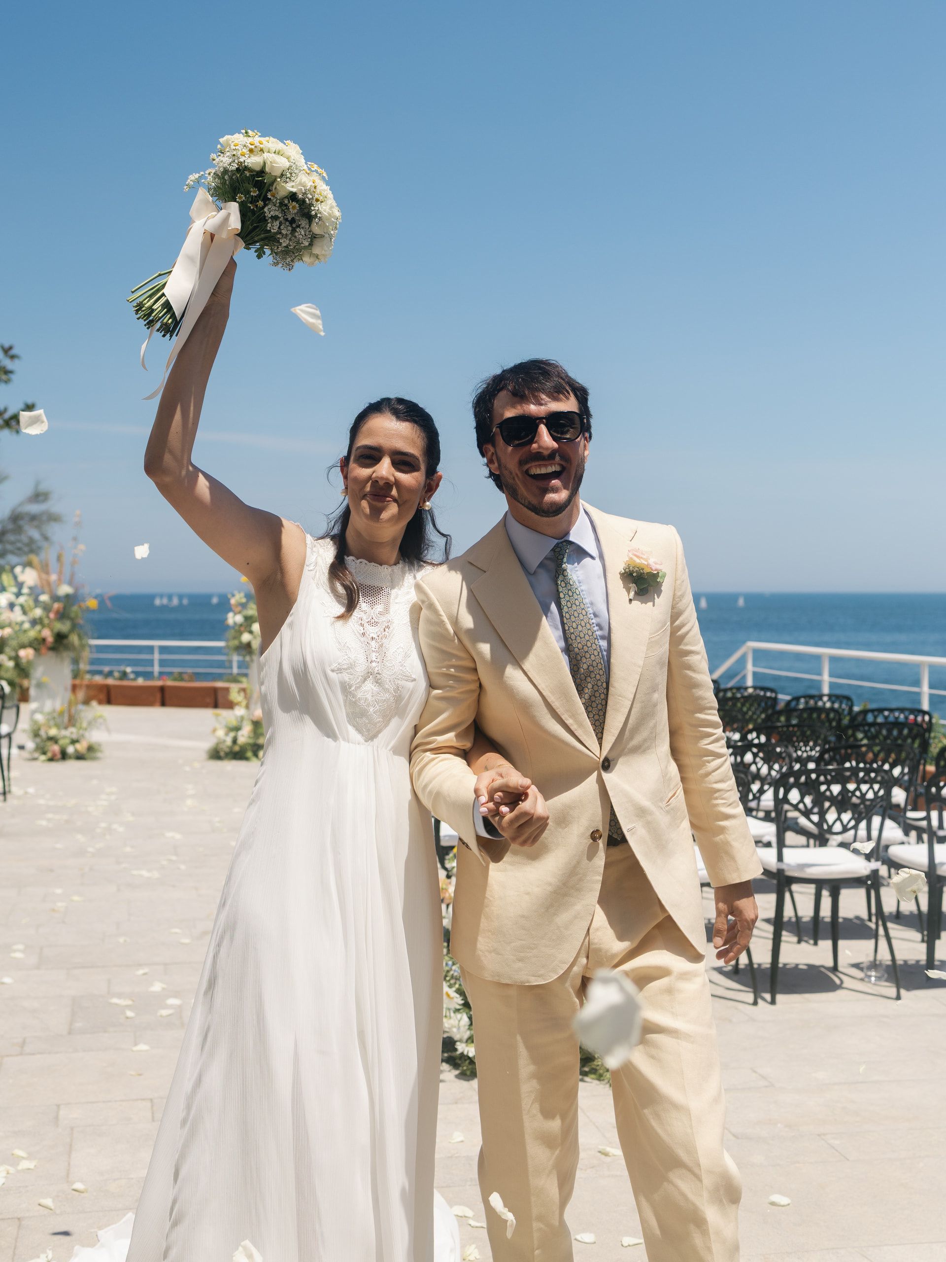 La sposa alza il bouquet in segno di festa accanto allo sposo, sulla terrazza sul mare