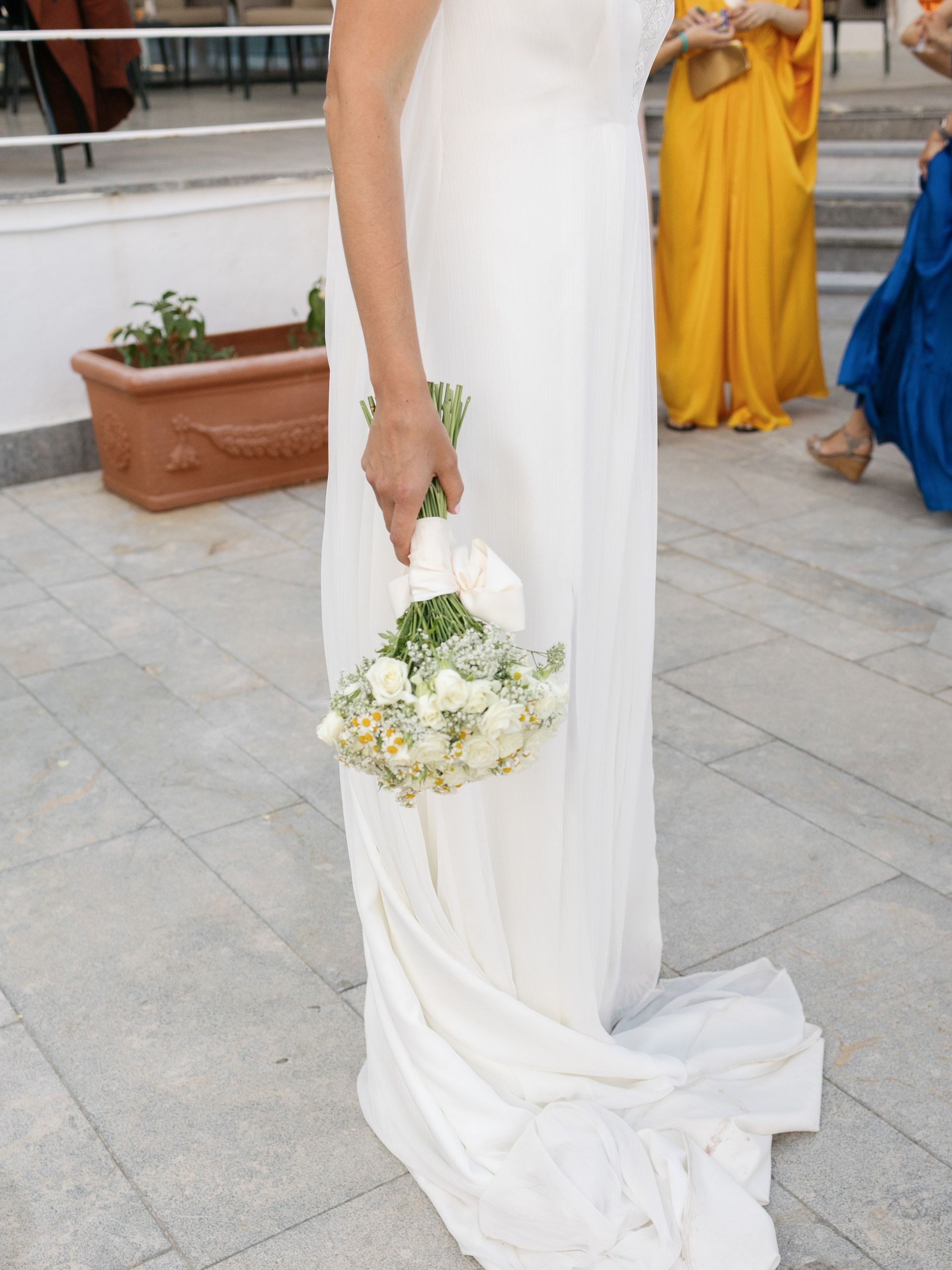 Il vestito della sposa e il bouquet bianco tenuto lungo il fianco, con lo strascico sul pavimento di pietra